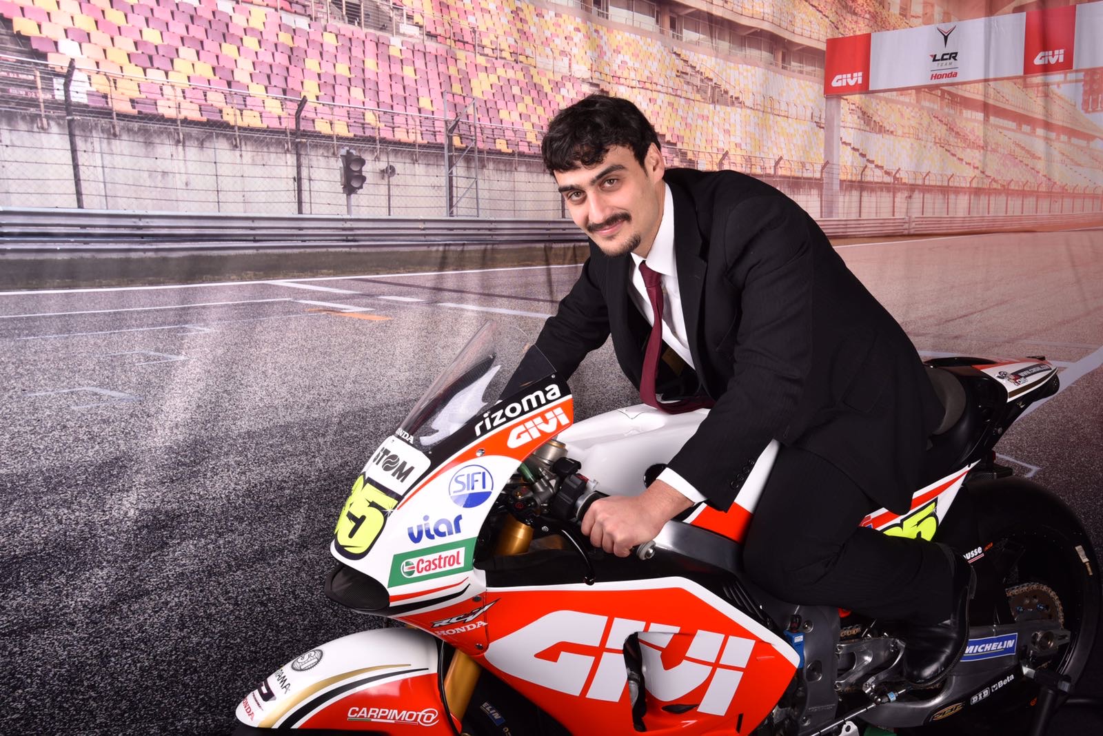 Francesco in giacca e cravatta su una moto da corsa Givi